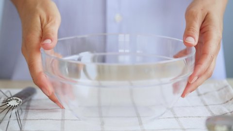 Close-up is a large glass bowl. Female hands pour sugar into a bowl for making a cake