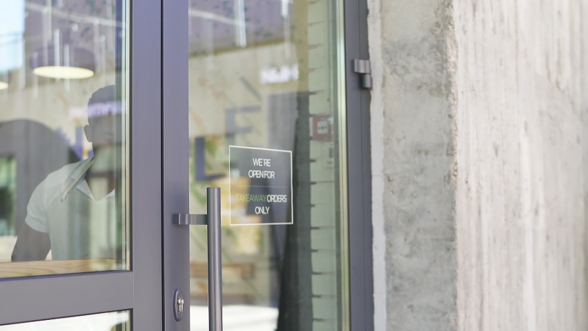 Handsome smiling man hold open sign in shop, stand near door and looks away, invite clients.