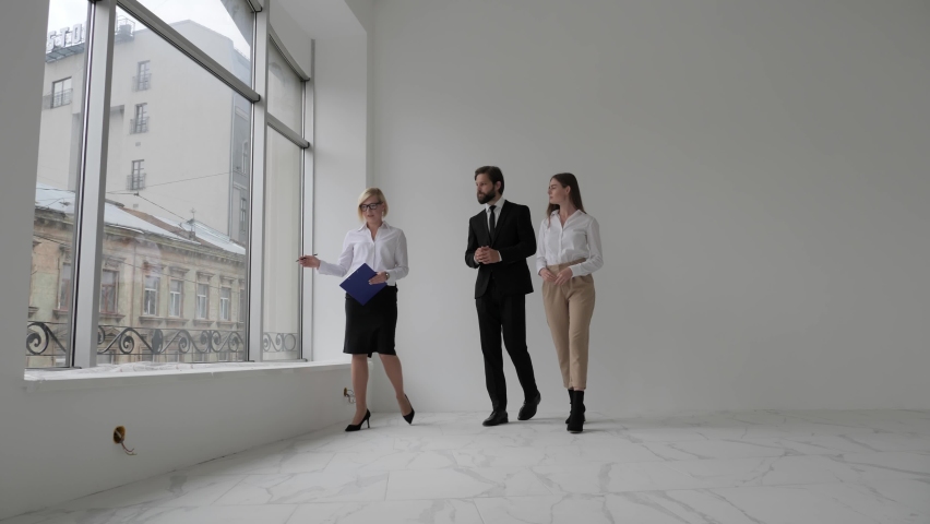 Real estate agent shows stylish modern office with panoramic windows to a beautiful young couple Purchasing/ Buying/ Renting Royalty-Free Stock Footage #1060473127