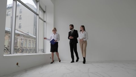 Real estate agent shows stylish modern office with panoramic windows to a beautiful young couple Purchasing/ Buying/ Renting