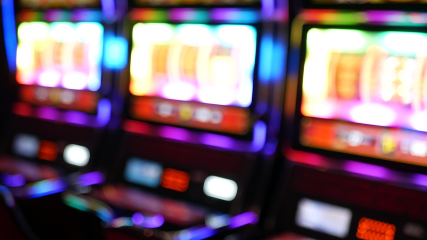 Defocused slot machines glow in casino on fabulous Las Vegas Strip, USA. Blurred gambling jackpot slots in hotel near Fremont street. Illuminated neon fruit machine for risk money playing and betting. Royalty-Free Stock Footage #1060474957