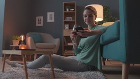 Happy young woman sitting on the floor in the living room, she is having a glass of wine and connecting online with her phone - Powered by Shutterstock - Get 15% off with code: PIKWIZARD15
