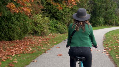 Beautiful girl wearing hat biking around Stanley Park by day during fall season in Vancouver, British Columbia, Canada. 