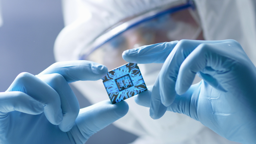 Futuristic Technology Concept: Engineer in Sterile Coverall Holds Computer Microchip with Gloves and Examines it. CPU Processor Digitalization with Data Lines Form Artificial Intelligence Symbol | Shutterstock HD Video #1060479019
