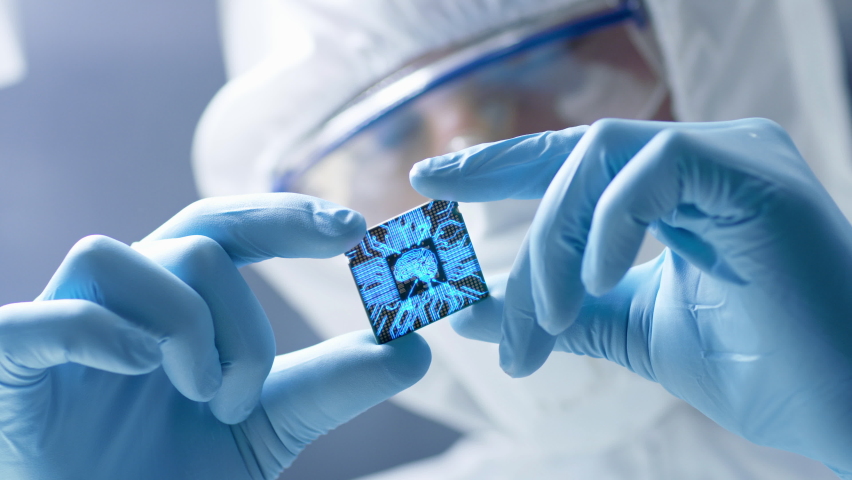 Futuristic Technology Concept: Engineer in Sterile Coverall Holds Computer Microchip with Gloves and Examines it. CPU Processor Digitalization with Data Lines Form Artificial Intelligence Symbol