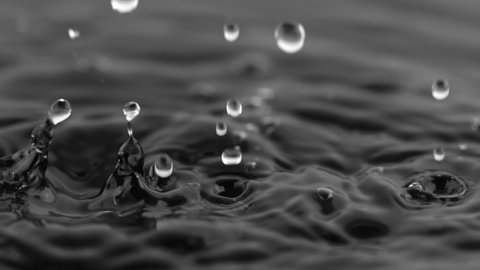 Super Slow Motion Shot of Water Drops Falling into Water on Black Background at 1000 fps.