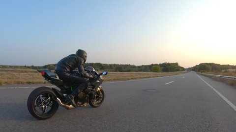 Aerial shot of man riding fast on modern sport motorbike at highway during sunset. Motorcyclist racing his motorcycle on country road. Guy driving bike during trip. Concept of freedom and adventure
