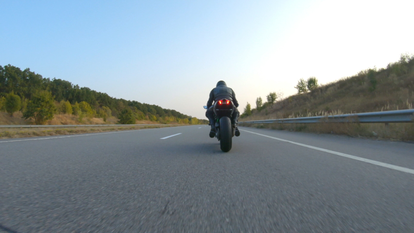 Biker is accelerating at motorcycle on empty country road. Man riding fast on modern sport motorbike at autumn highway. Guy driving bike during trip. Concept of freedom and adventure. Aerial shot Royalty-Free Stock Footage #1060484605