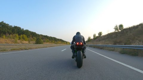 Biker is accelerating at motorcycle on empty country road. Man riding fast on modern sport motorbike at autumn highway. Guy driving bike during trip. Concept of freedom and adventure. Aerial shot