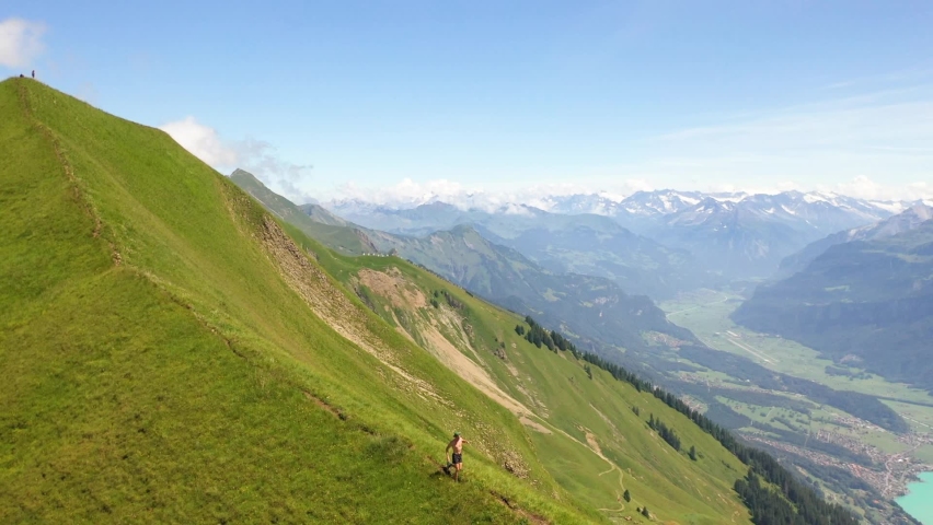 Aerial shot circling around counter-clockwise a young white male running alone by himself on a ridge at Interlaken, Switzerland. Fantastic and beautiful scenery around him.