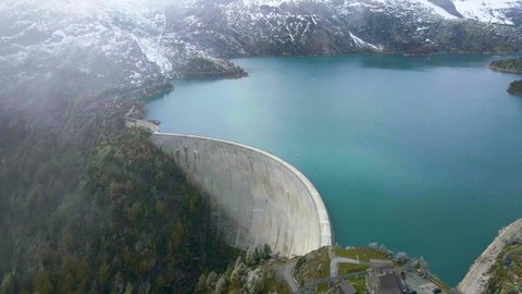 Arch dam and reservoir lake in Swiss Alps mountains feeding hydropower electric power plant to produce renewable energy, sustainable hydroelectricity, snowy weather, aerial drone footage 4K 60 fps