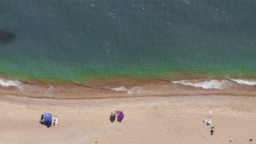 Top down view of unrecognizable people sunbathing at beautiful turquoise blue sea beach top aerial angle. Umbrellas and towels. People relaxing on sand