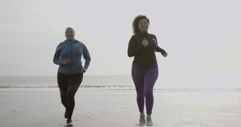 Mother and daughter running exercising outdoors on beach, black women sports training body positive