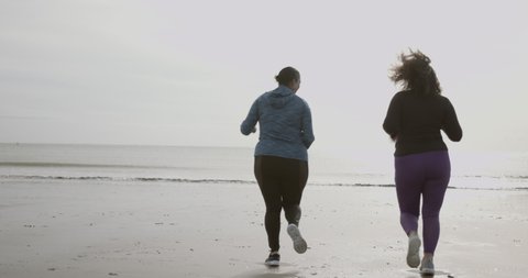 Two plus size females running exercising outdoors on beach, black women sports training body positive