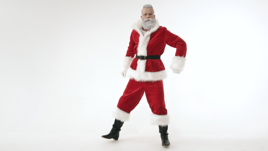 Active Cheerful Stylish Santa Claus Positively Dances, Haves Fun to Energetic Music Looking at Camera, Standing on White Background Indoors. Joyful Celebration Happy New Year, Merry Christmas Holidays Royalty-Free Stock Footage #1060490467
