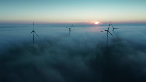 Wind turbines at sunrise in heavy fog. Wind farm generating green energy