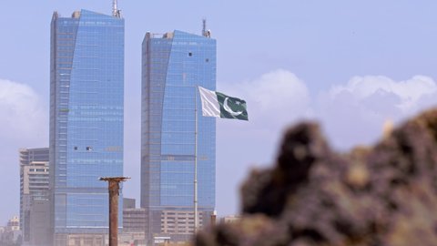 Unique view of Pakistan National flag (Public Property) waving in front of the Tall office buildings - slow-mo shot.
