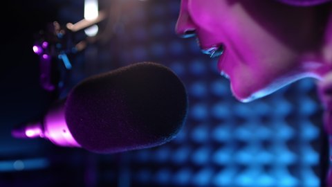 Beautiful young female dj speaks into microphone, records podcast or morning news show for radio. Close up of podcast presenter or DJ talking on the microphone. Wears professional headphones