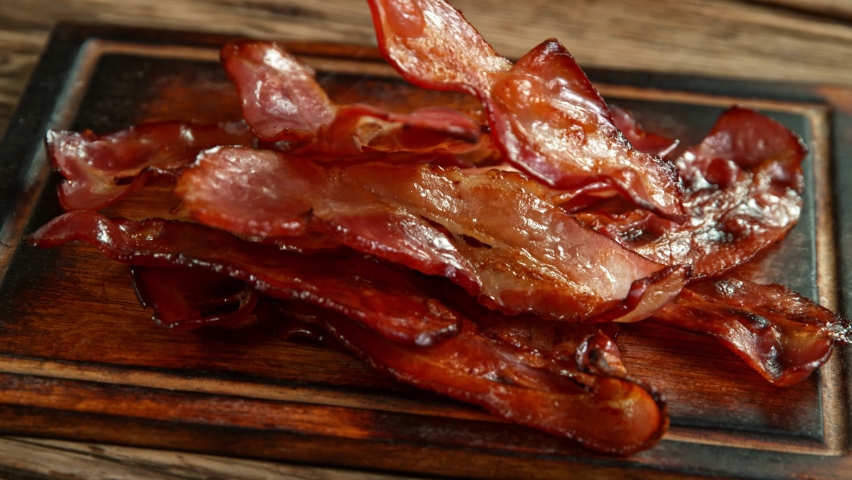 Super Slow Motion Shot of Roasted Bacon Slices Falling on Wooden Board at 1000 fps. Royalty-Free Stock Footage #1060495804