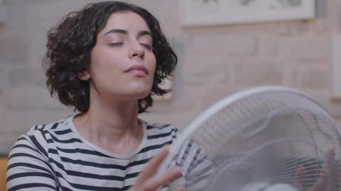 Woman suffering from the summer heat and trying to cool off with her fan. A sweaty woman is disturbed by the air conditioner malfunction in the humidity concept.