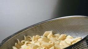 The pasta was cooked in the restaurant's kitchen.Pasta is mixed in a pan in the restaurant kitchen. Mixing pasta in a metal strainer. Slow motion and close up video.