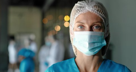 Portrait of tired Caucasian pretty woman doctor in hat and medical mask looking at camera. Close up of female physician. Medic or nurse in clinic. Indoor. Coronavirus concept. Protected.