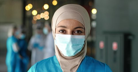 Portrait of Arab woman doctor in hijab and medical mask standing in hospital. Close up of muslim female medic in traditional headscarf in clinic. Covid-19. Arabian nurse. Coronavirus concept.