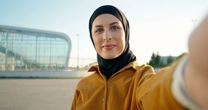 POV of young muslim beautiful woman in traditional headscarf standing outdoor and talking via web cam. Videochat concept. Pretty girl with covered head waving with hand to camera and videochatting.