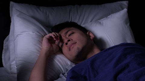 Depressed young Asian man cannot sleep from insomnia. Depressed man suffering from insomnia lying in bed.