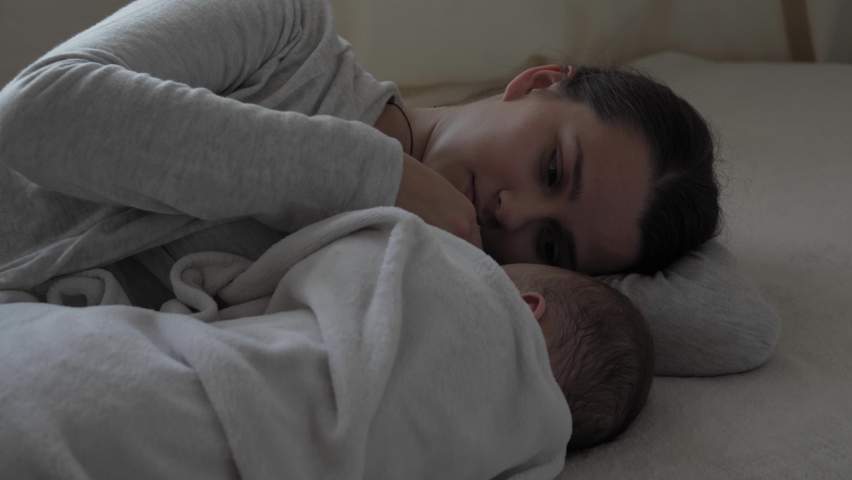 A young happy mother lay near a sleepy 7 month baby girl covered warm blanket and sing lullaby sit in the nursery on soft bed. Royalty-Free Stock Footage #1060506256