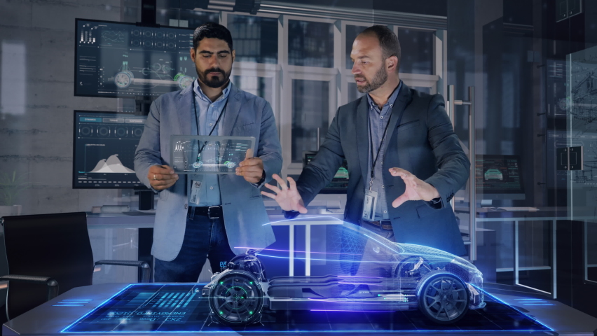 Professional Male Automotive Designers makes gestures and redesigns 3D Electric Concept Car Model using Holographic Table. High Tech Office use Virtual Augmented Reality Modeling Software Application.