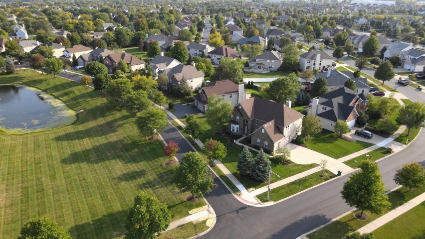 Overhead aerial view of colorful trees, residential houses and yards with drainage pond along suburban street in Chicago area. Midwest USA Royalty-Free Stock Footage #1060507615