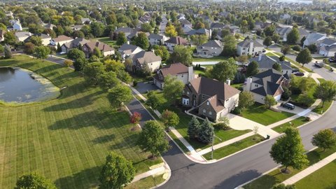 Overhead aerial view of colorful trees, residential houses and yards with drainage pond along suburban street in Chicago area. Midwest USA