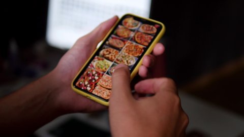 Ordering pizza using online delivery. A man orders food at home in an online store using a smartphone. Ordering pizza using a food delivery app. Online delivery, online store, home delivery.