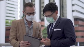 Business people Caucasian with Asian man colleague partnership wearing protective face mask for protect covid-19 virus discussing business project plan with using digital tablet computer in the city - Powered by Shutterstock - Get 15% off with code: PIKWIZARD15
