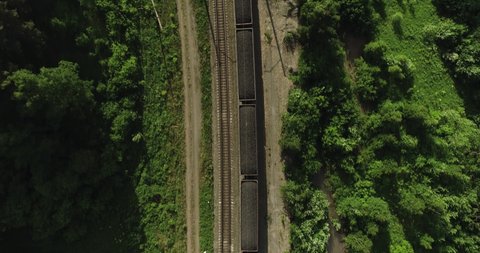 Freight long train carries with coal carriages an electric locomotive by dangerous part of two-sided Trans Siberian railways in forest mountains / Aerial drone wide view at summer sunny day