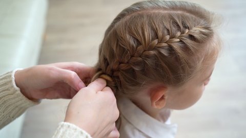 mom's hands braid her daughter's pigtails for school in the morning. care of children's hair.