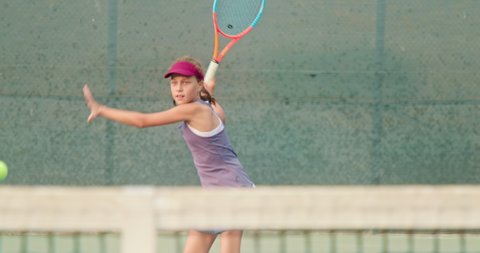 Athletic girl playing tennis game on the court. Active teenager is hitting the ball by the colorful racket. Young sportsman during the sport match. Slow motion female is practicing tennis game 4K, USA