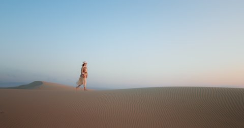 Cinematic footage with copy space on light blue background in soft sunset light. Scenic landscape view with plain nature background for commercial text. Woman walking by sand dune and desert scenery