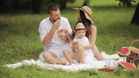 Parents and their son eating bakery at picnic.