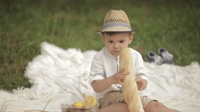 A little caucasian boy with pretty face eats an yummy baguette in the park