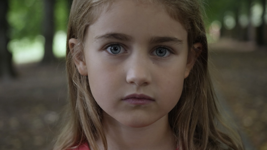 Portrait Little Child Girl Looking at Camera Standing on Street in City on Summer Day. Young Sad Thinking Curiosity Child Looking at Camera Closeup Outdoors. Face Eyes Serious Contemplative Child. | Shutterstock HD Video #1060522093