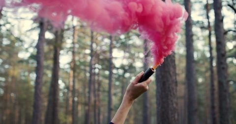 woman's hand with red smoke grenade in forest. slow motion.