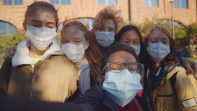 Multiethnic school children wearing protective face mask taking selfie outdoors. Happy diverse classmates making photos together standing outside school building in safety mask - Powered by Shutterstock - Get 15% off with code: PIKWIZARD15