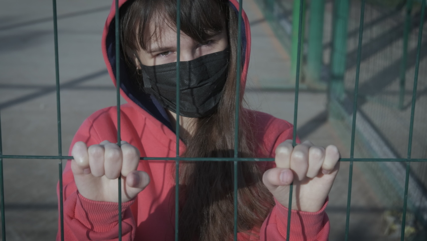 Life in quarantine. Restriction of freedom in quarantine. The masked girl loosens the iron mesh. Royalty-Free Stock Footage #1060526632