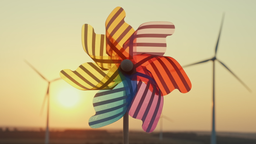 Pinwheel rotate color plastic, windmill blowing wind against  of wind turbines wind park sunset sky of sunny day summer. Descending bright disk of sun beyond horizon on field. Alternative energy Royalty-Free Stock Footage #1060527745