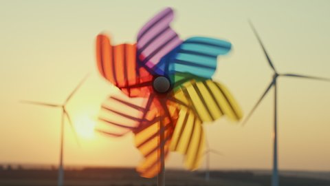 Pinwheel rotate color plastic, windmill blowing wind against  of wind turbines wind park sunset sky of sunny day summer. Descending bright disk of sun beyond horizon on field. Alternative energy