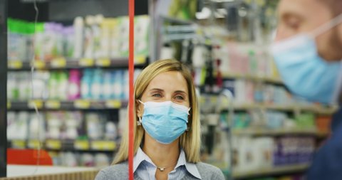 Authentic shot of female customer and male cashier wearing medical masks to protect themselves from disease while paying with credit card grocery food products in supermarket.