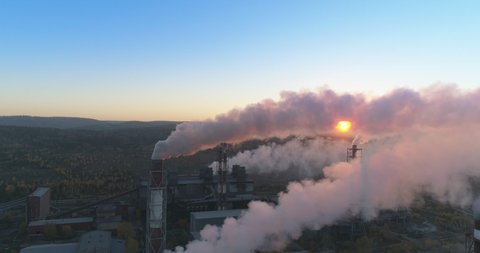 Aerial drone footage of steel factory pipes during sunset time. high above metallurgical plant and smoke cloud is coming from chimney. Aerial 4K