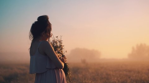 pregnant stands in foggy field looking at the sunrise flowers in her hands